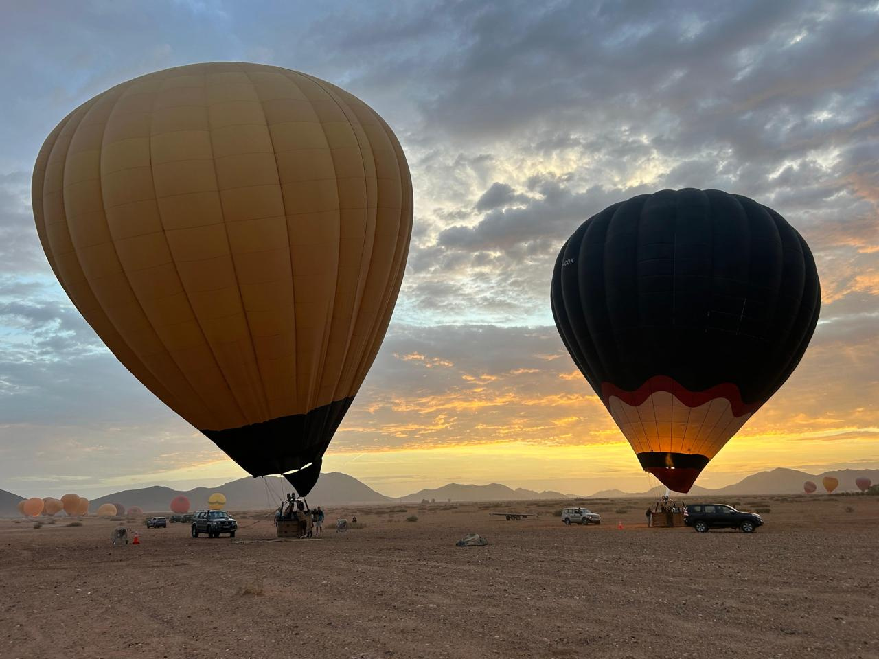 Two hot air balloons rising in dramatic morning light above Marrakech plains